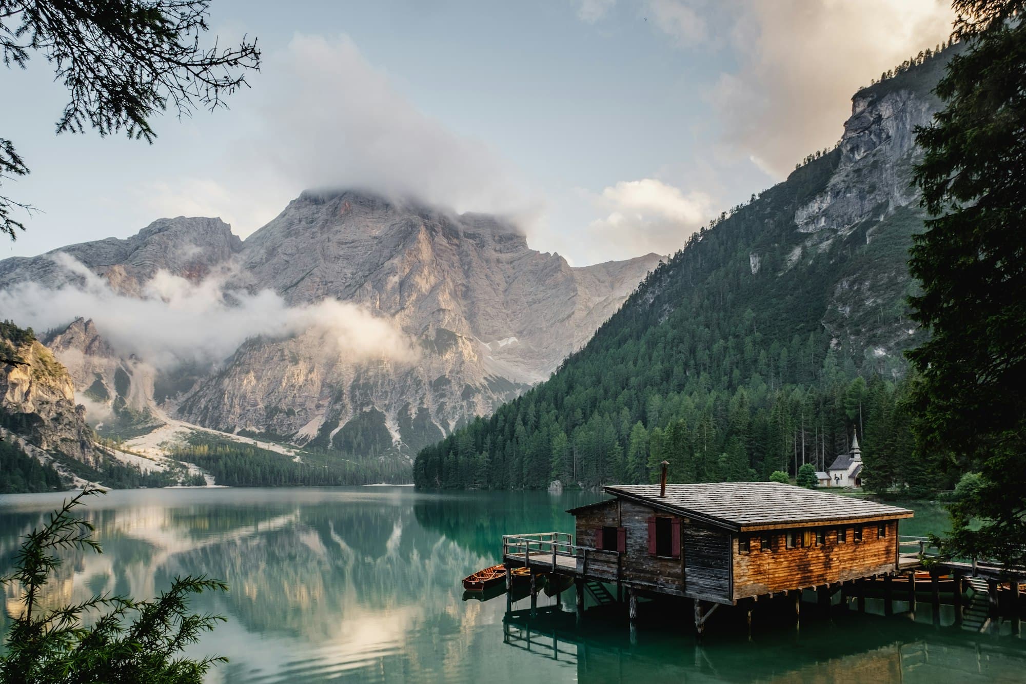 A cabin on an alpine lake beneath a misty mountain